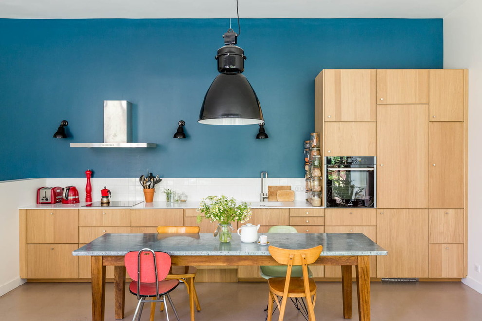 パリにある北欧スタイルのおしゃれなキッチン (フラットパネル扉のキャビネット、淡色木目調キャビネット、白いキッチンパネル、黒い調理設備、茶色い床、白いキッチンカウンター) の写真