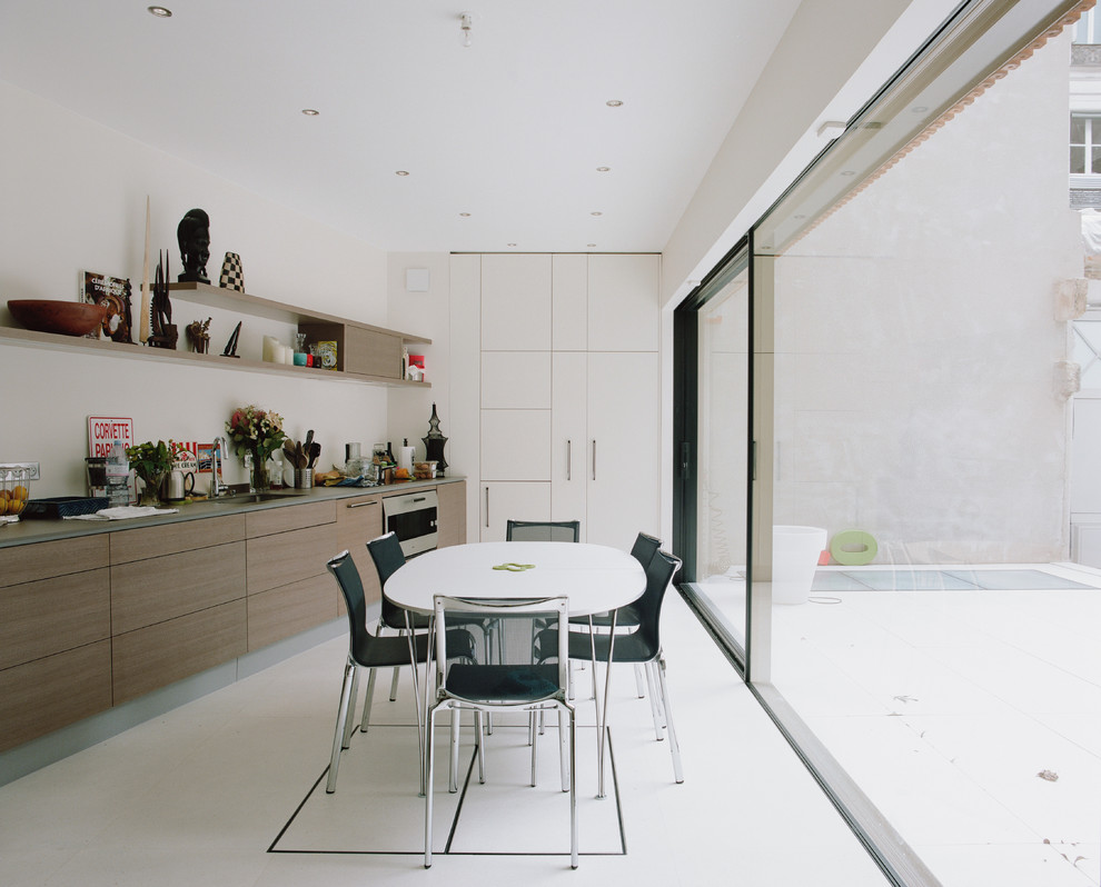 Moderne Wohnküche in L-Form mit Unterbauwaschbecken, flächenbündigen Schrankfronten, hellbraunen Holzschränken, Küchenrückwand in Weiß, Küchengeräten aus Edelstahl, weißem Boden und grauer Arbeitsplatte in Paris