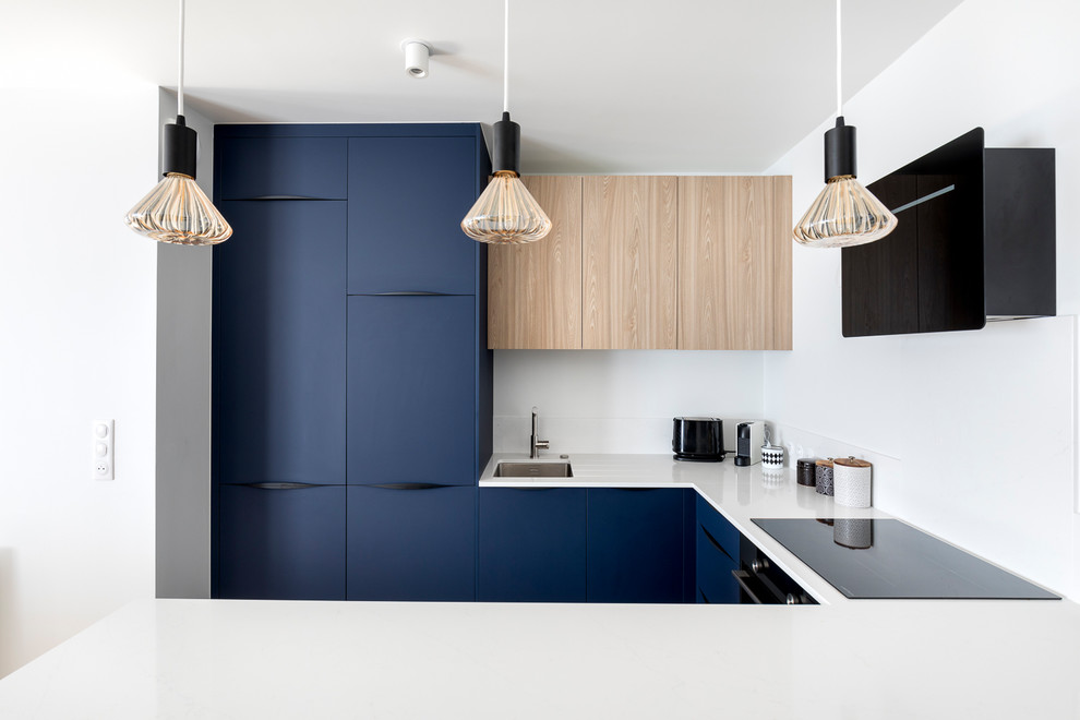 Inspiration for a medium sized nautical u-shaped open plan kitchen in Paris with a single-bowl sink, flat-panel cabinets, blue cabinets, composite countertops, white splashback, marble splashback, black appliances, light hardwood flooring, an island and white worktops.