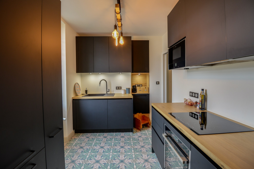 Cette image montre une petite cuisine encastrable design en U fermée avec un plan de travail en bois, carreaux de ciment au sol et des portes de placard grises.