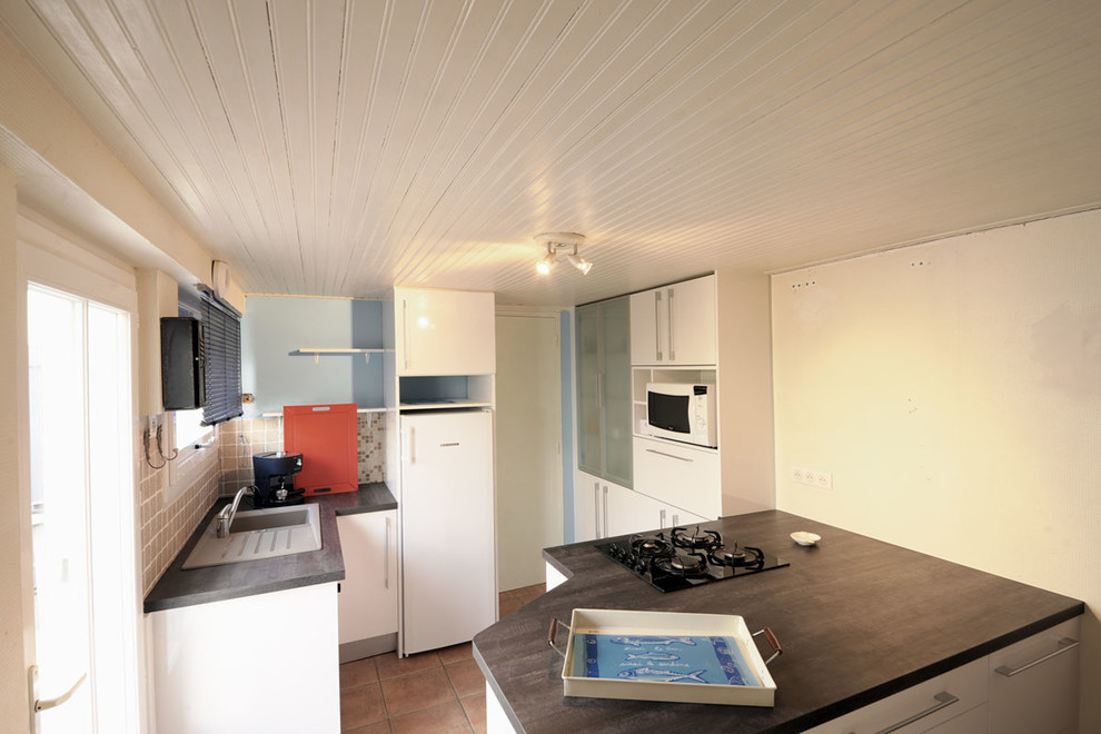 Moderne Küche mit weißen Schränken, Laminat-Arbeitsplatte, Küchenrückwand in Beige, Rückwand aus Terrakottafliesen, Terrakottaboden, Kücheninsel und orangem Boden in Nantes