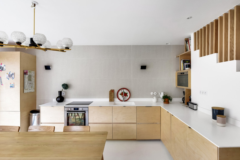 Moderne Wohnküche ohne Insel in L-Form mit integriertem Waschbecken, flächenbündigen Schrankfronten, hellen Holzschränken, Küchenrückwand in Grau, Elektrogeräten mit Frontblende und grauem Boden in Paris