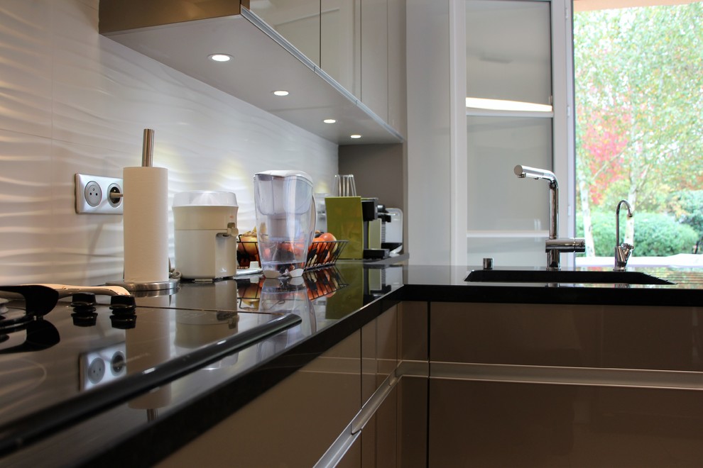 Inredning av ett modernt stort u-kök, med en undermonterad diskho, grå skåp, granitbänkskiva, vitt stänkskydd och rostfria vitvaror