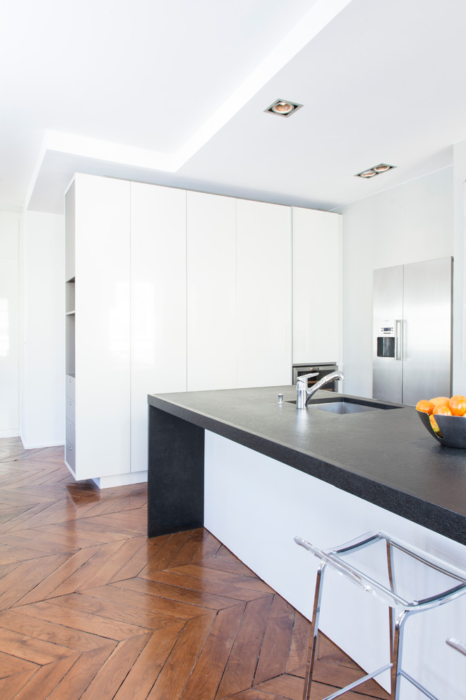 Medium sized contemporary galley kitchen/diner in Lyon with a submerged sink, beaded cabinets, white cabinets, granite worktops, stainless steel appliances, dark hardwood flooring and an island.