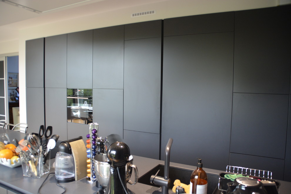 Cette image montre une cuisine américaine parallèle design avec un évier intégré, un placard à porte affleurante, des portes de placard grises, un électroménager noir, parquet clair et îlot.