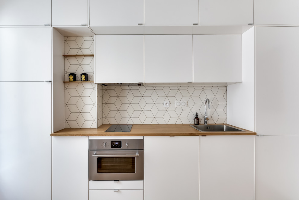 Bild på ett litet skandinaviskt linjärt kök och matrum, med vita skåp, träbänkskiva, vitt stänkskydd, stänkskydd i keramik, ljust trägolv, en nedsänkt diskho, släta luckor och rostfria vitvaror