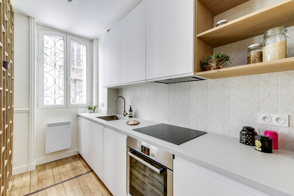 Foto på ett skandinaviskt grå linjärt kök, med en nedsänkt diskho, släta luckor, vita skåp, vitt stänkskydd, rostfria vitvaror, ljust trägolv och beiget golv