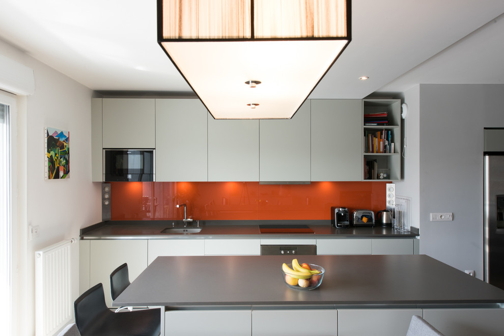 Idéer för ett mellanstort modernt kök, med orange stänkskydd, glaspanel som stänkskydd, en köksö, en undermonterad diskho, släta luckor, vita skåp och integrerade vitvaror