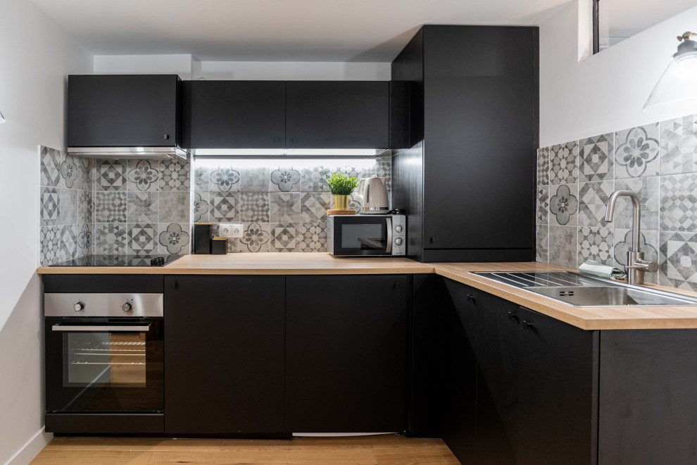 Small trendy l-shaped brown floor kitchen photo in Paris with a drop-in sink, flat-panel cabinets, black cabinets, wood countertops, multicolored backsplash, stainless steel appliances, no island and beige countertops