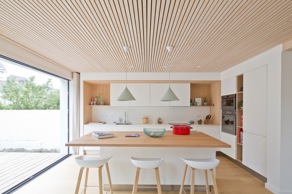 Inspiration for a medium sized nautical l-shaped kitchen/diner in Rennes with a submerged sink, white cabinets, engineered stone countertops, white splashback, integrated appliances, light hardwood flooring, an island, white worktops, flat-panel cabinets, metro tiled splashback and brown floors.