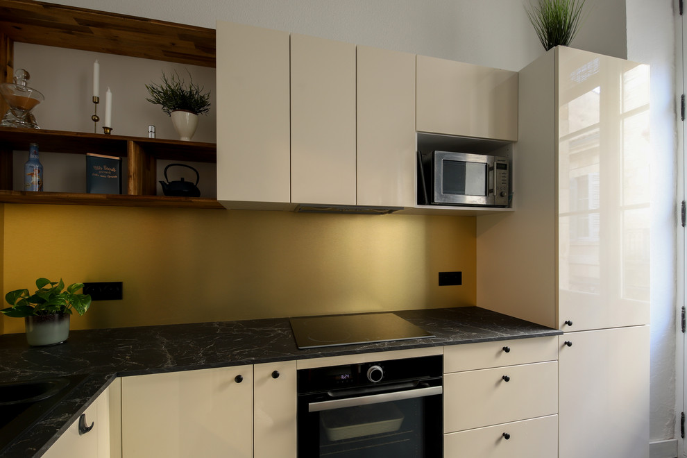 This is an example of a small eclectic u-shaped kitchen/diner in Bordeaux with a single-bowl sink, beige cabinets, laminate countertops, yellow splashback, black appliances, laminate floors, an island, black floors and black worktops.