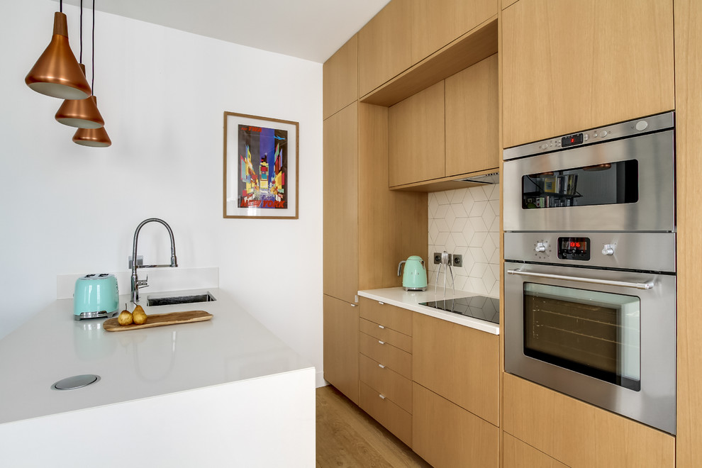 パリにある高級な小さなコンテンポラリースタイルのおしゃれなキッチン (アンダーカウンターシンク、フラットパネル扉のキャビネット、中間色木目調キャビネット、白いキッチンパネル、シルバーの調理設備、無垢フローリング) の写真