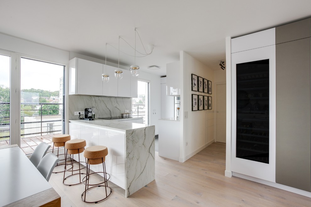 Photo of a medium sized contemporary l-shaped kitchen/diner in Paris with an integrated sink, beaded cabinets, granite worktops, white splashback, stainless steel appliances, light hardwood flooring, a breakfast bar and white worktops.