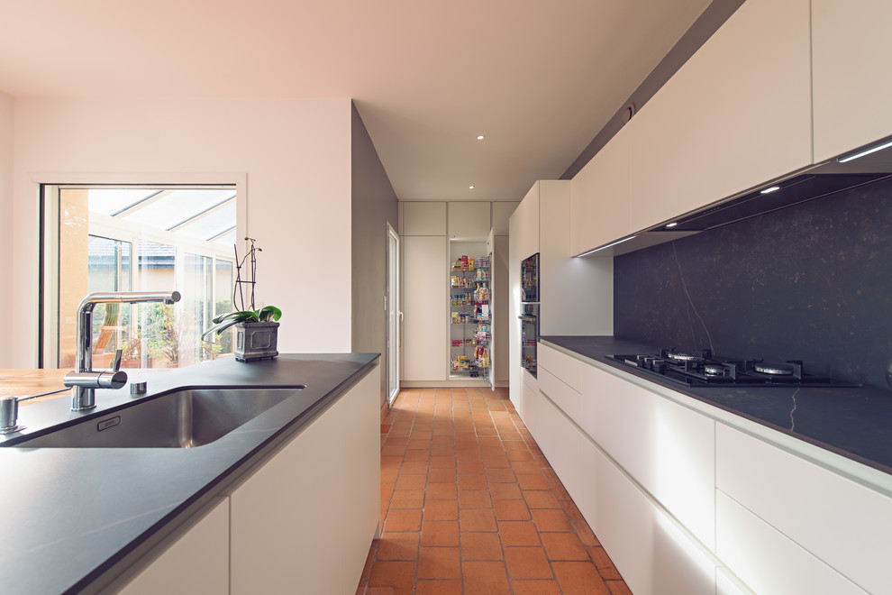 Photo of a large contemporary galley open plan kitchen in Rennes with a single-bowl sink, flat-panel cabinets, white cabinets, ceramic splashback, stainless steel appliances, terracotta flooring and multiple islands.