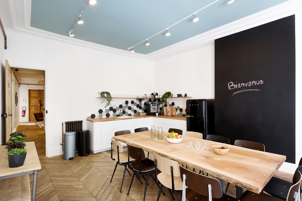 Inspiration for a scandinavian l-shaped light wood floor and beige floor eat-in kitchen remodel in Paris with a drop-in sink, flat-panel cabinets, white cabinets, wood countertops, multicolored backsplash, black appliances, no island and beige countertops
