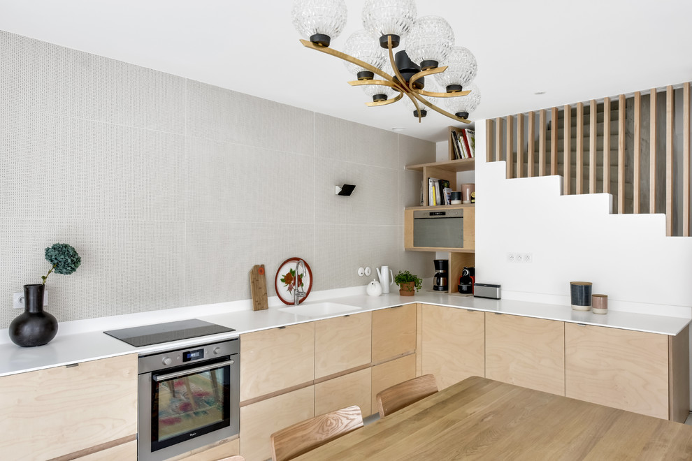 Bild på ett mellanstort funkis kök, med en integrerad diskho, släta luckor, skåp i ljust trä, rostfria vitvaror, bänkskiva i rostfritt stål, vitt stänkskydd och ljust trägolv