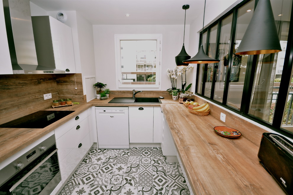 Cette photo montre une cuisine industrielle avec un évier encastré, un placard à porte plane, des portes de placard blanches, un plan de travail en bois, une crédence marron, un électroménager noir, carreaux de ciment au sol et un sol gris.