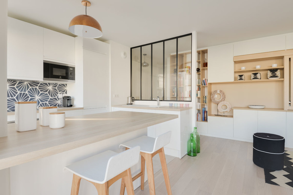 Inspiration for a mid-sized scandinavian l-shaped ceramic tile and beige floor eat-in kitchen remodel in Paris with a single-bowl sink, flat-panel cabinets, white cabinets, wood countertops, blue backsplash, cement tile backsplash, stainless steel appliances and an island