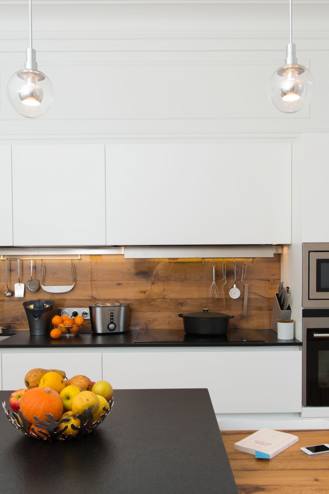 Cette photo montre une cuisine parallèle tendance de taille moyenne avec un placard à porte plane, des portes de placard blanches, une crédence marron, un électroménager en acier inoxydable et îlot.