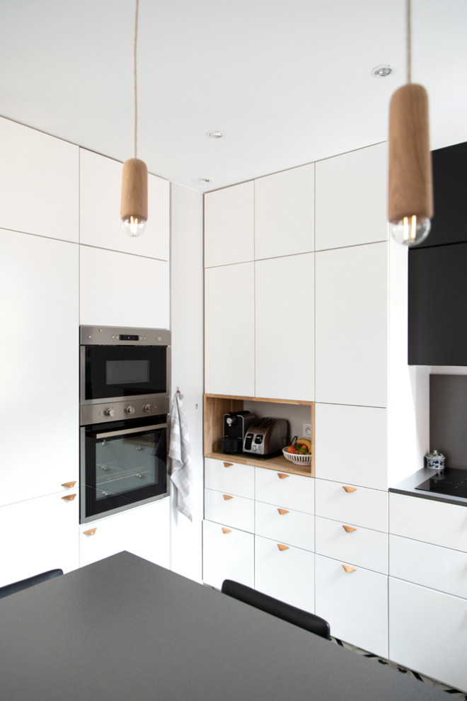 This is an example of a large classic u-shaped enclosed kitchen in Paris with a submerged sink, beaded cabinets, white cabinets, laminate countertops, black splashback, stone slab splashback, integrated appliances, cement flooring, a breakfast bar, multi-coloured floors and black worktops.