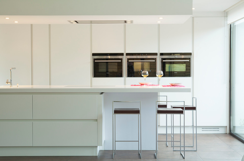 Foto de cocina comedor contemporánea grande con fregadero integrado, armarios con paneles lisos, puertas de armario blancas, encimera de acrílico, electrodomésticos con paneles y una isla
