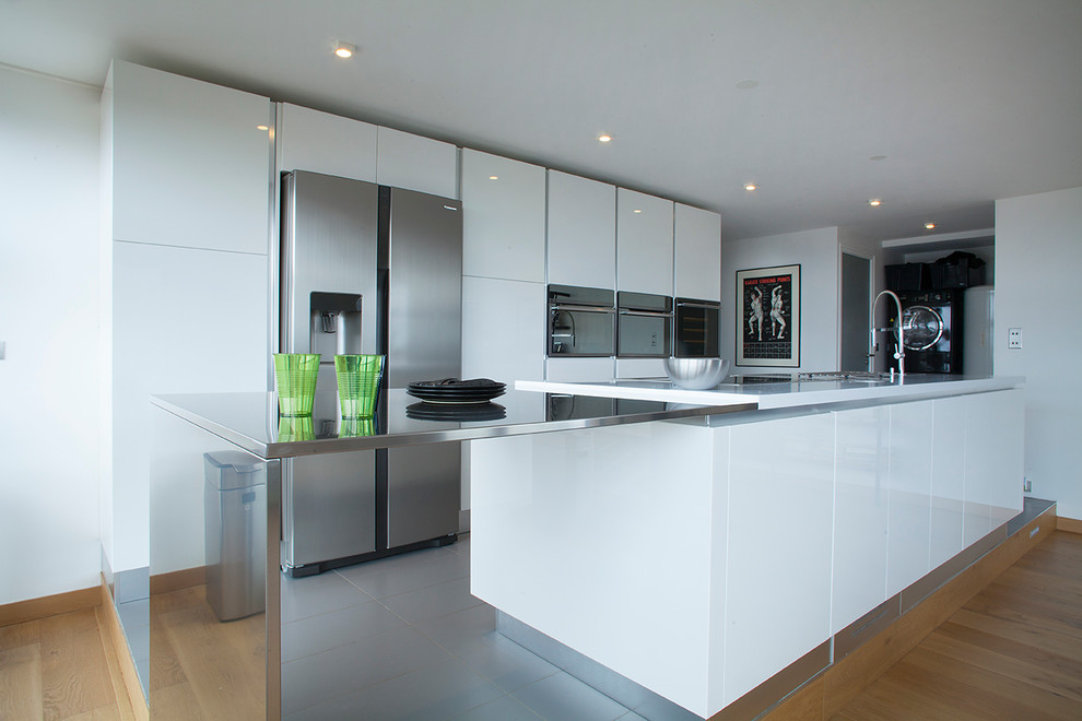 Eat-in kitchen - large contemporary galley gray floor eat-in kitchen idea in Lille with an undermount sink, flat-panel cabinets, white cabinets, solid surface countertops, stainless steel appliances and an island
