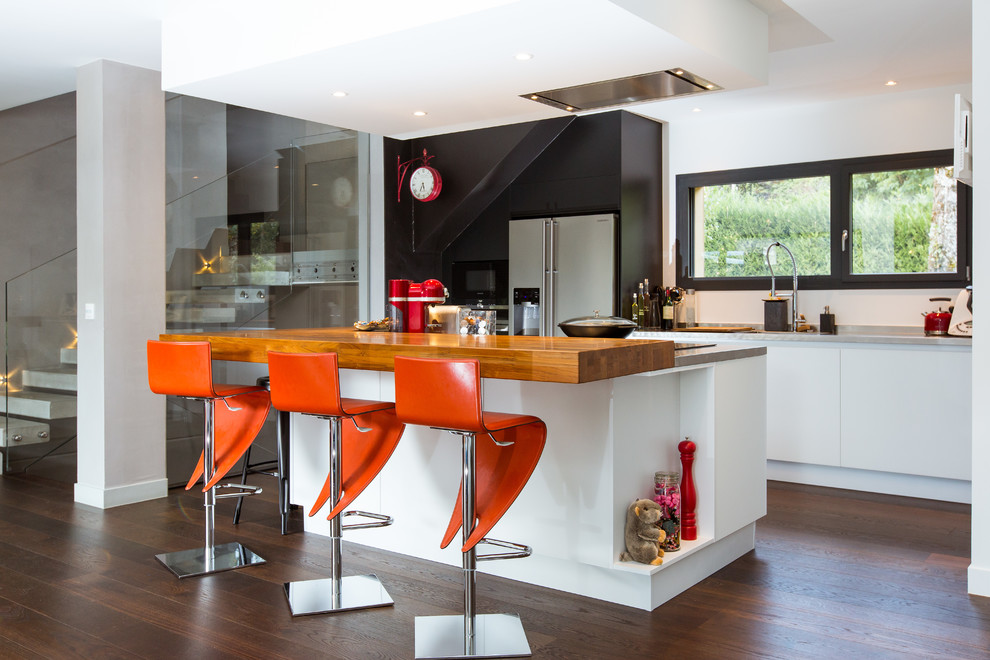 Immagine di una cucina design con lavello sottopiano, ante lisce, ante bianche, elettrodomestici in acciaio inossidabile, parquet scuro e pavimento marrone