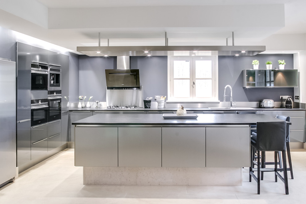 Moderne Küche mit Einbauwaschbecken, flächenbündigen Schrankfronten, grauen Schränken, Küchengeräten aus Edelstahl, Kücheninsel und beigem Boden in Dijon