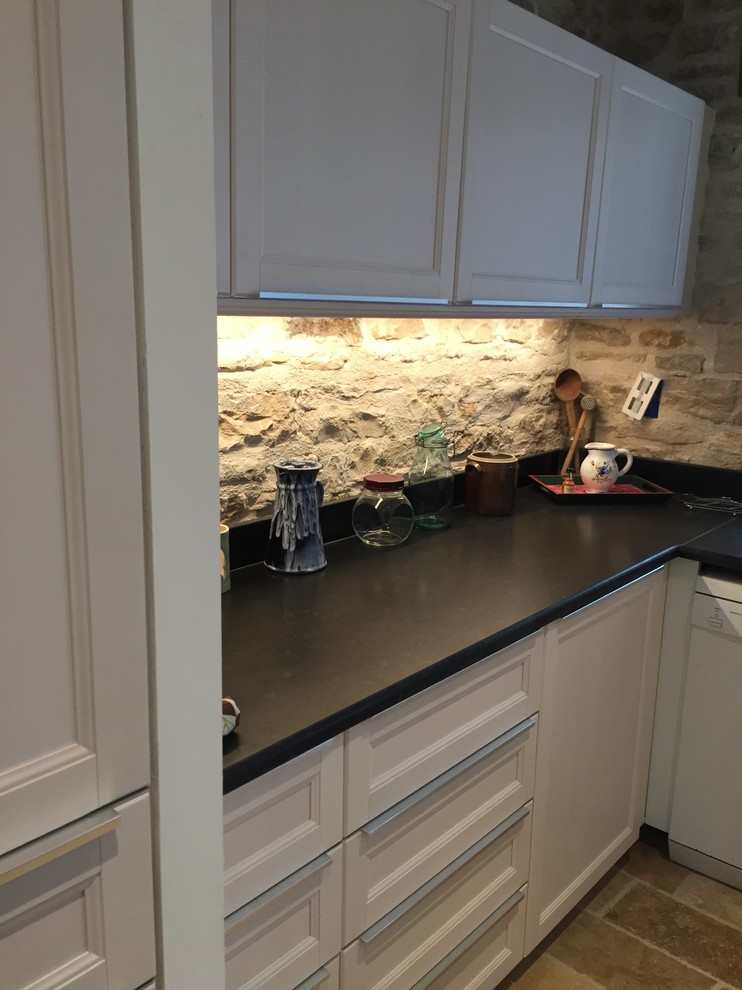 Cette photo montre une cuisine ouverte nature en L avec des portes de placard blanches, une crédence beige, une crédence en pierre calcaire et un sol beige.