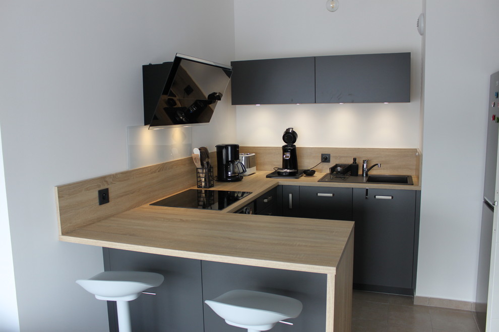 Photo of a small contemporary u-shaped kitchen/diner in Lyon with a submerged sink, beaded cabinets, grey cabinets, laminate countertops, beige splashback, wood splashback, black appliances, ceramic flooring, a breakfast bar, brown floors and beige worktops.