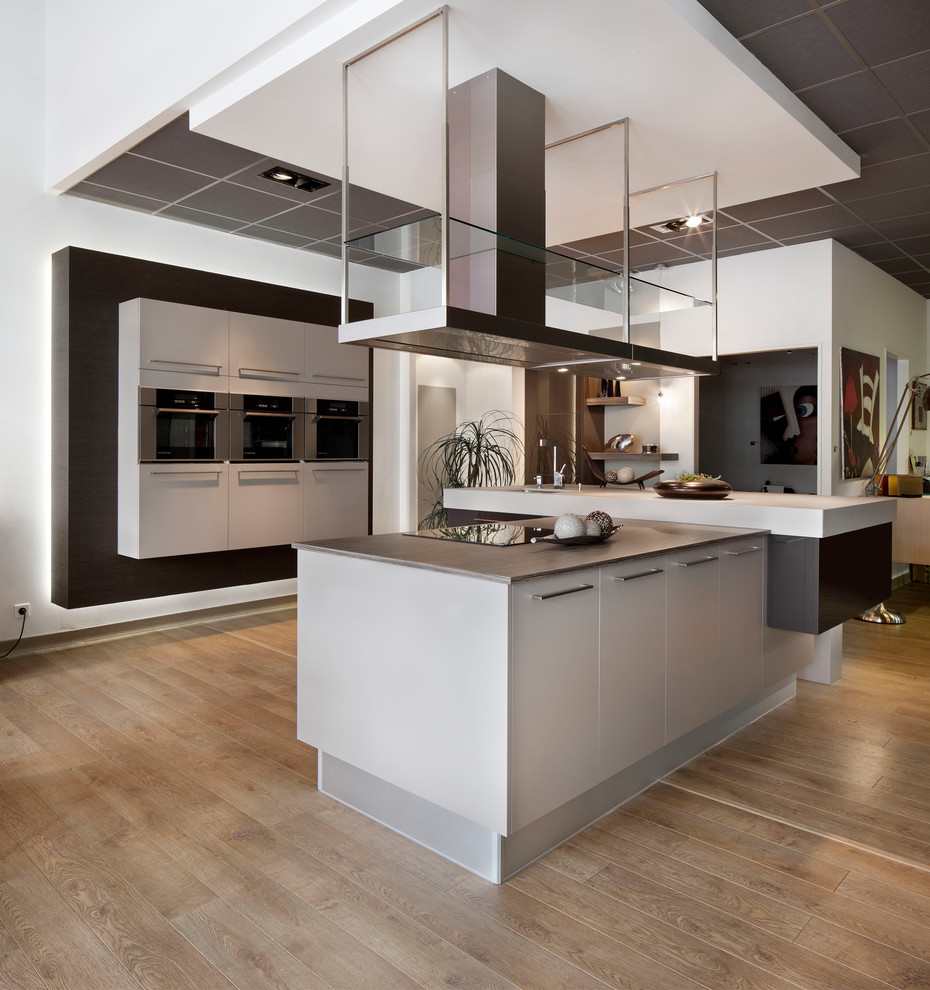 Ejemplo de cocina contemporánea grande abierta con fregadero integrado, puertas de armario blancas, encimera de laminado, electrodomésticos con paneles, suelo de madera clara y una isla