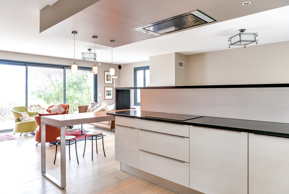 Large modern l-shaped kitchen/diner in Lyon with flat-panel cabinets, medium wood cabinets, granite worktops, a breakfast bar, a submerged sink, orange splashback, wood splashback, stainless steel appliances, light hardwood flooring, beige floors and grey worktops.