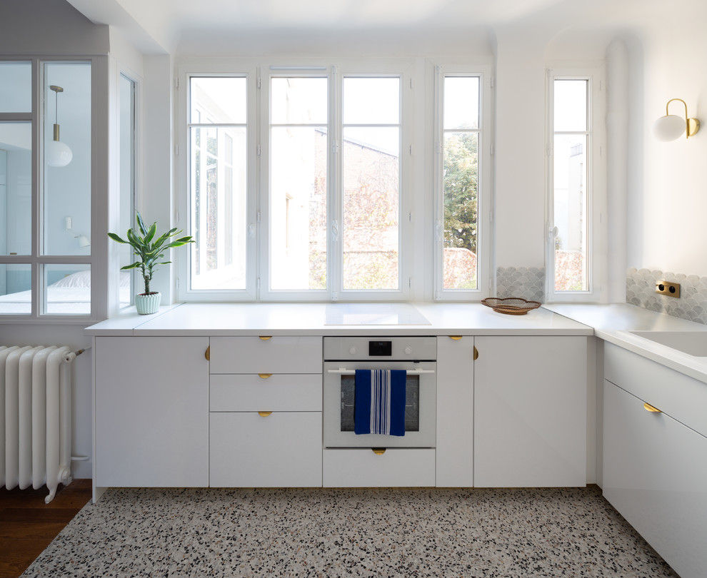 Bild på ett mellanstort funkis vit vitt kök, med en undermonterad diskho, luckor med profilerade fronter, vita skåp, laminatbänkskiva, grått stänkskydd, stänkskydd i marmor, vita vitvaror, terrazzogolv och grått golv