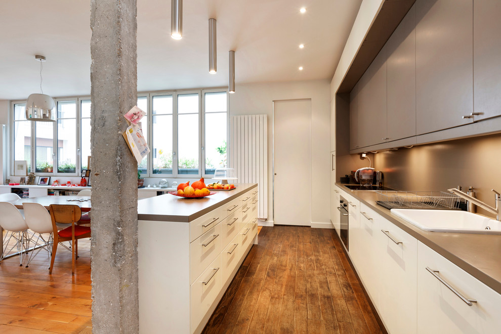 Zweizeilige, Große Moderne Wohnküche mit Einbauwaschbecken, flächenbündigen Schrankfronten, weißen Schränken, braunem Holzboden und Kücheninsel in Paris