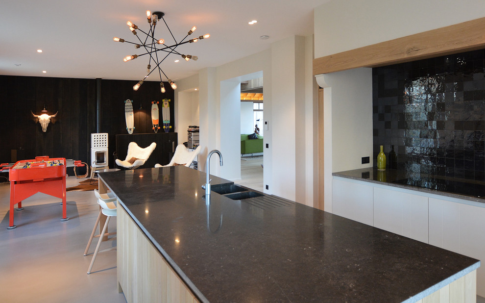 Cette image montre une grande cuisine américaine parallèle design en bois clair avec un placard à porte affleurante, un plan de travail en granite, une crédence noire et îlot.