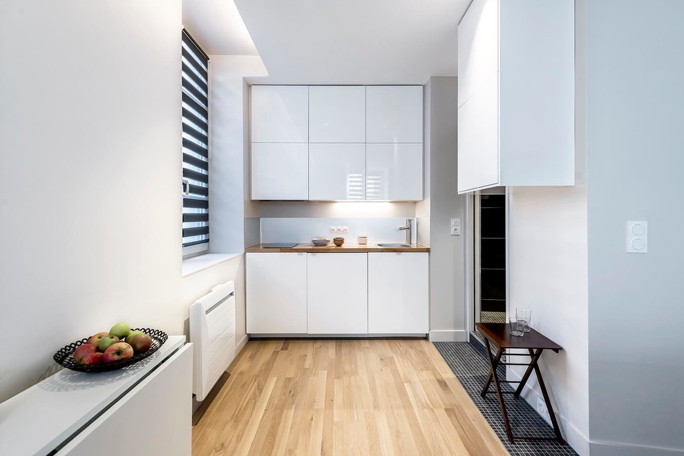 Inspiration för små moderna linjära kök med öppen planlösning, med en nedsänkt diskho, vita skåp, träbänkskiva, stänkskydd med metallisk yta, stänkskydd i metallkakel och ljust trägolv