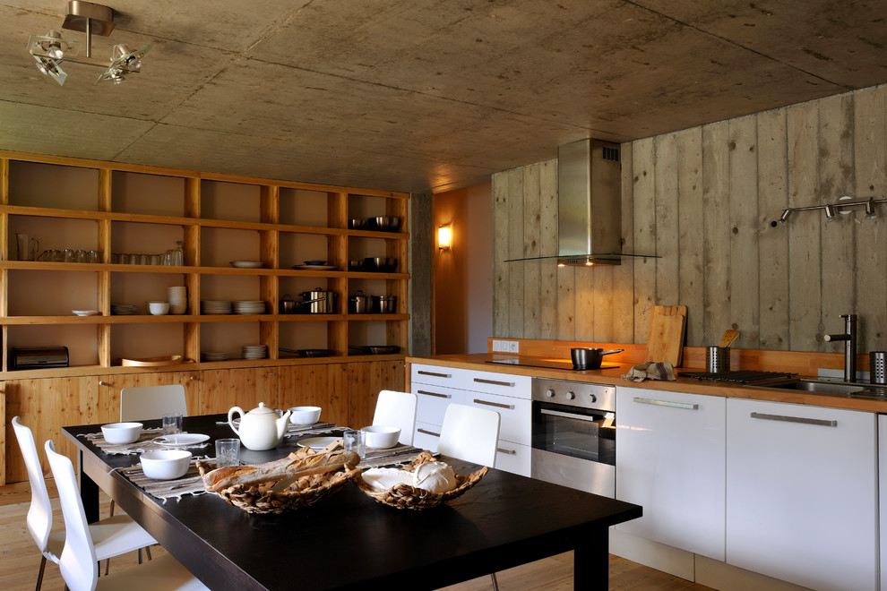 Große Eklektische Wohnküche ohne Insel in L-Form mit flächenbündigen Schrankfronten, weißen Schränken, Arbeitsplatte aus Holz, braunem Holzboden und Mauersteinen in Lyon