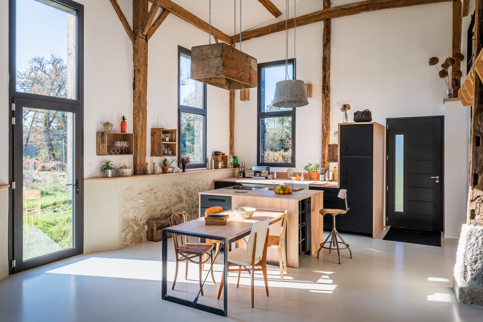 Inspiration for a farmhouse galley open plan kitchen in Bordeaux with a belfast sink, flat-panel cabinets, black cabinets, wood worktops, integrated appliances, concrete flooring, an island, grey floors and beige worktops.