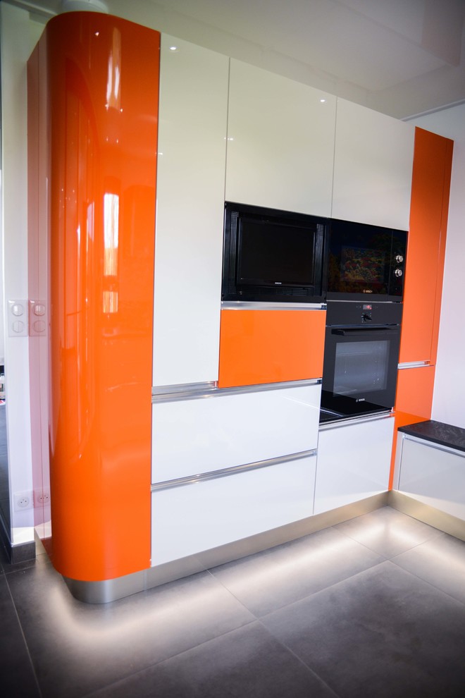 Modern inredning av ett avskilt, mellanstort u-kök, med en integrerad diskho, luckor med profilerade fronter, orange skåp, laminatbänkskiva, svart stänkskydd, färgglada vitvaror, klinkergolv i keramik och svart golv