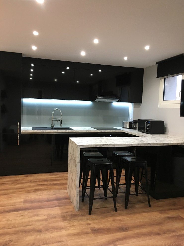 Bild på ett litet funkis flerfärgad flerfärgat kök, med en enkel diskho, luckor med profilerade fronter, svarta skåp, laminatbänkskiva, grått stänkskydd, glaspanel som stänkskydd, integrerade vitvaror, plywoodgolv, en köksö och brunt golv
