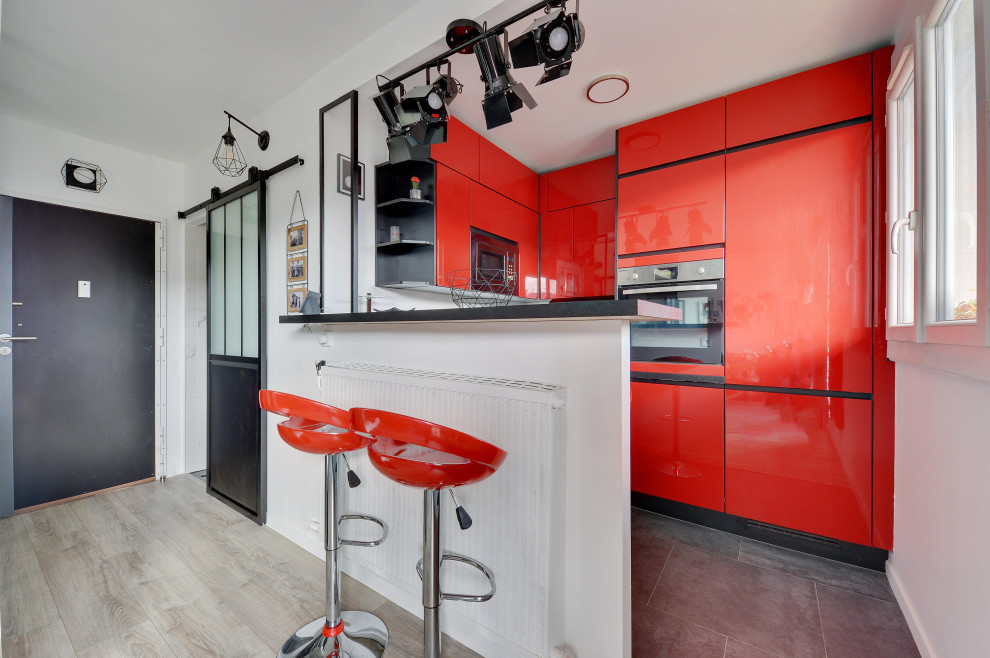 Cette photo montre une cuisine tendance en U avec un placard à porte plane, des portes de placard rouges, un électroménager en acier inoxydable, une péninsule et un sol gris.