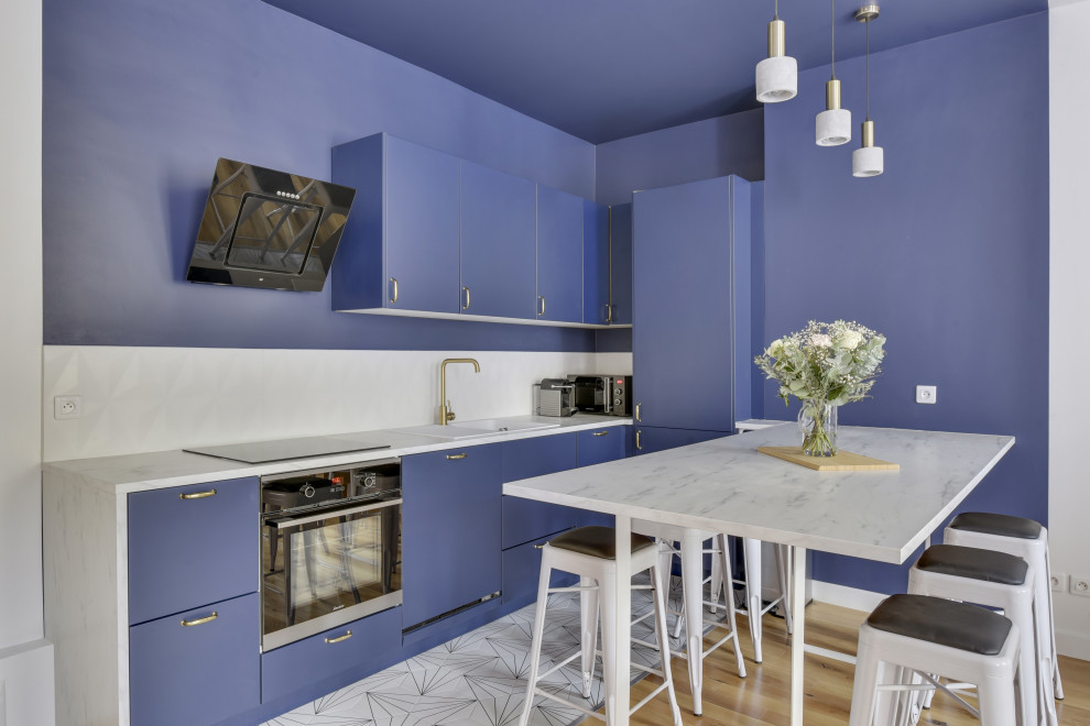 Moderne Wohnküche ohne Insel in L-Form mit Einbauwaschbecken, flächenbündigen Schrankfronten, blauen Schränken, Küchenrückwand in Weiß, Küchengeräten aus Edelstahl, weißem Boden und weißer Arbeitsplatte in Paris