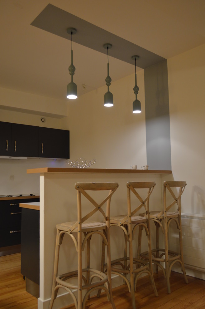 Cette image montre une cuisine ouverte design en U avec des portes de placard noires, un plan de travail en bois, un électroménager en acier inoxydable, sol en stratifié, un sol blanc et un plan de travail beige.