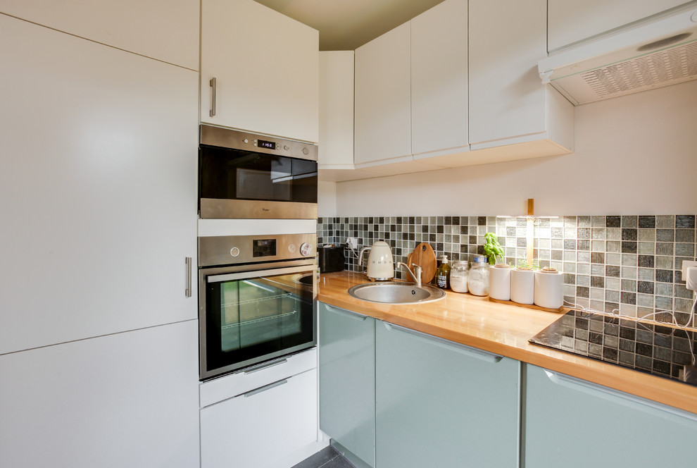 Bild på ett litet minimalistiskt kök, med en undermonterad diskho, släta luckor, gröna skåp, träbänkskiva, grönt stänkskydd, stänkskydd i keramik, integrerade vitvaror, skiffergolv och grått golv