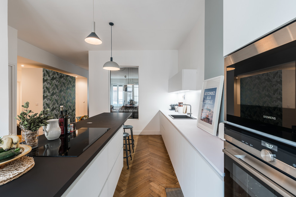 Example of a large trendy galley dark wood floor enclosed kitchen design in Lyon with a single-bowl sink, white cabinets, laminate countertops, stainless steel appliances and an island