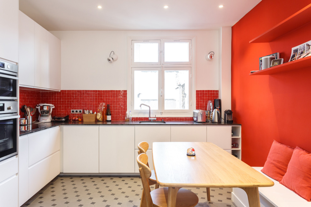パリにあるお手頃価格の広いモダンスタイルのおしゃれなキッチン (アンダーカウンターシンク、フラットパネル扉のキャビネット、白いキャビネット、クオーツストーンカウンター、赤いキッチンパネル、テラコッタタイルのキッチンパネル、シルバーの調理設備、セラミックタイルの床、アイランドなし、マルチカラーの床、黒いキッチンカウンター) の写真