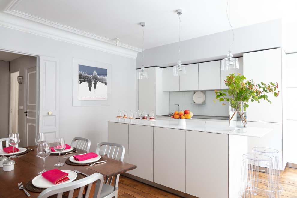 Cette image montre une cuisine américaine nordique avec un placard à porte plane, des portes de placard blanches, une crédence grise, parquet clair, îlot et un plan de travail gris.