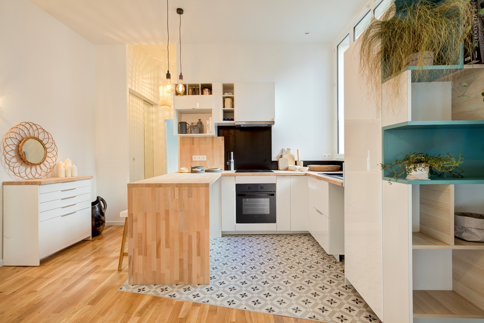 Inspiration för ett mellanstort funkis kök, med en undermonterad diskho, vita skåp, träbänkskiva, svart stänkskydd, integrerade vitvaror, cementgolv, flerfärgat golv, en halv köksö och släta luckor
