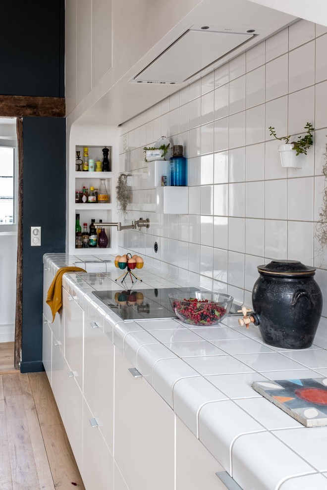 Foto de cocina lineal contemporánea de tamaño medio abierta sin isla con armarios con paneles lisos, puertas de armario blancas, encimera de azulejos, salpicadero blanco, salpicadero de azulejos de porcelana, electrodomésticos con paneles, suelo de madera clara, suelo beige, encimeras blancas y fregadero bajoencimera