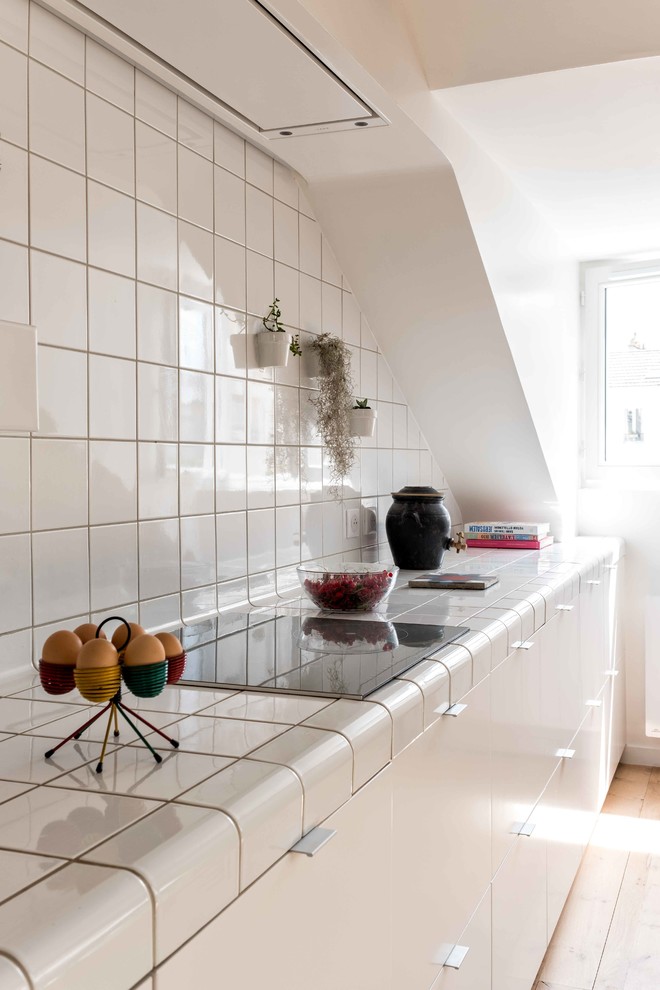 Photo of a medium sized contemporary single-wall open plan kitchen in Paris with flat-panel cabinets, white cabinets, tile countertops, white splashback, porcelain splashback, integrated appliances, light hardwood flooring, beige floors, white worktops, a submerged sink and no island.